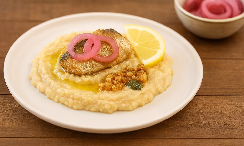 Creamy mashed white beans topped with flaky tinned mackerel and pink pickled onions, served on a rustic wooden counter with a lemon wedge.