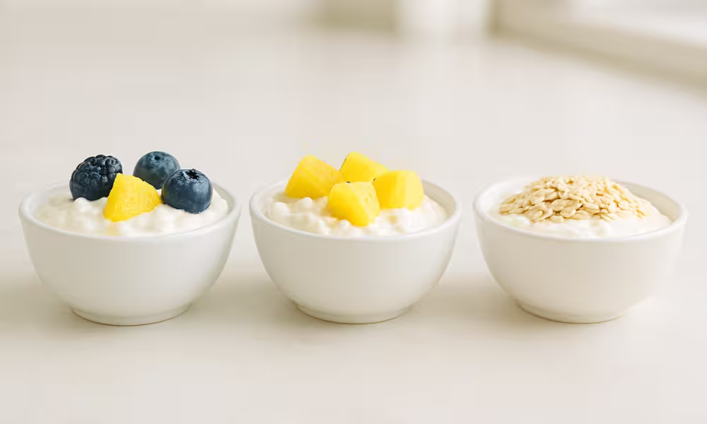“Bowls of Greek yogurt with berries, cottage cheese with pineapple, and skyr with oats on a kitchen counter in natural light.”