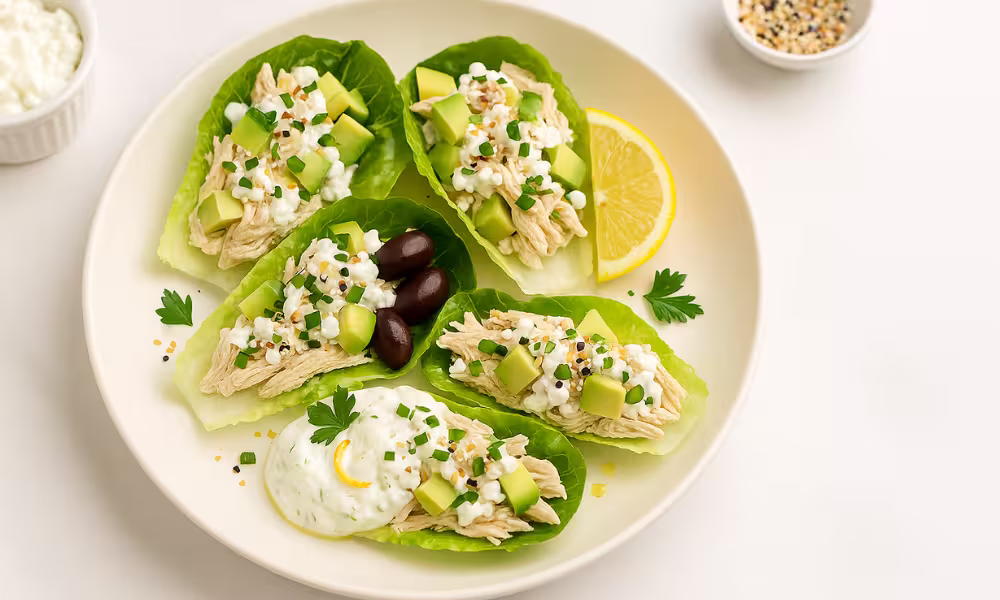 “No-cook chicken and cottage-cheese lettuce wraps with avocado and chives, sprinkled with everything bagel seasoning, lemon wedge on white marble.”