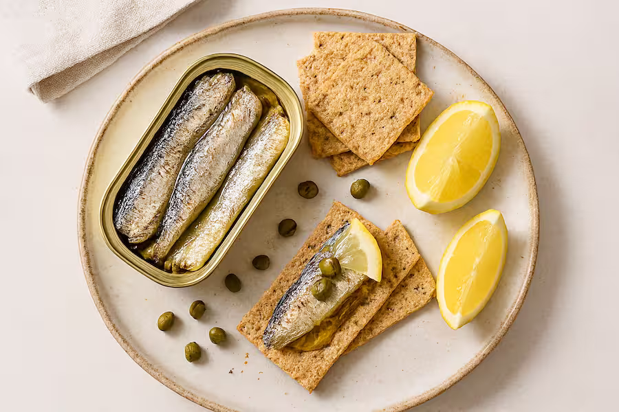 “High-protein snack with sardines, lemon, capers, and whole-grain crackers on a rustic plate.”